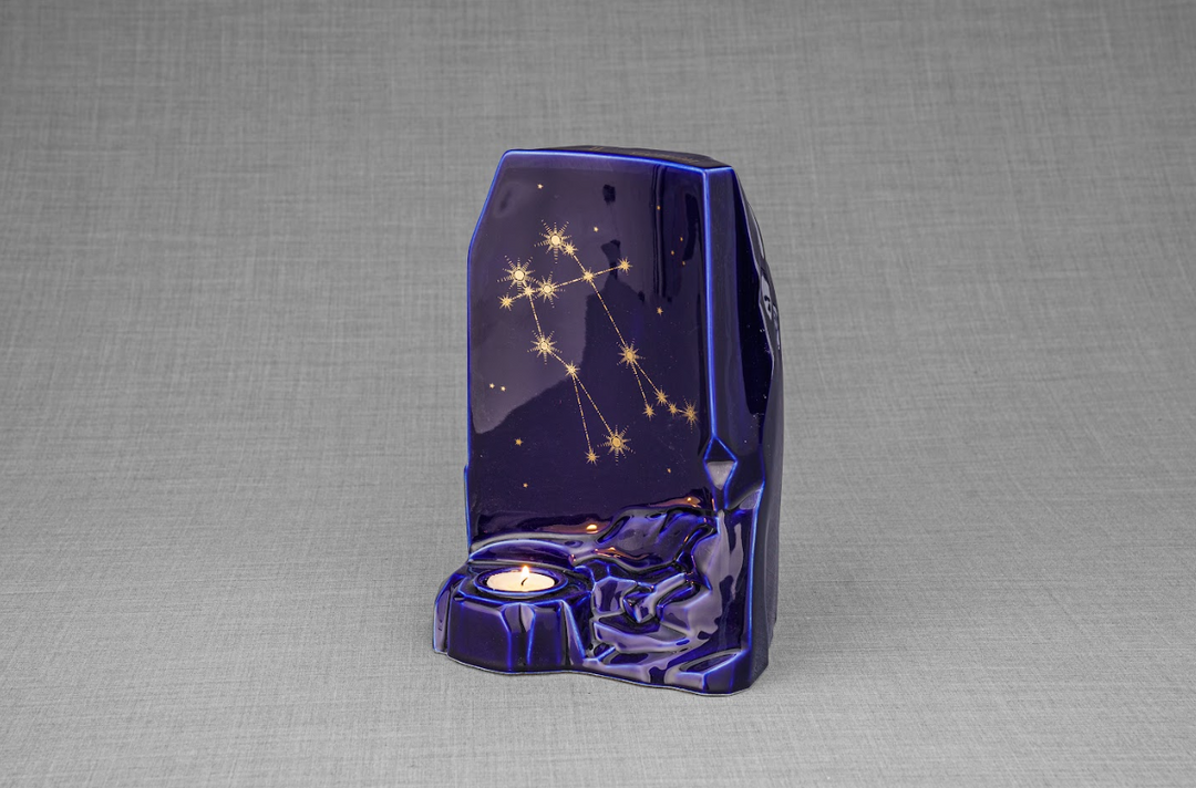 Deep blue ceramic urn with gold constellation lines and a candle-lit base.
