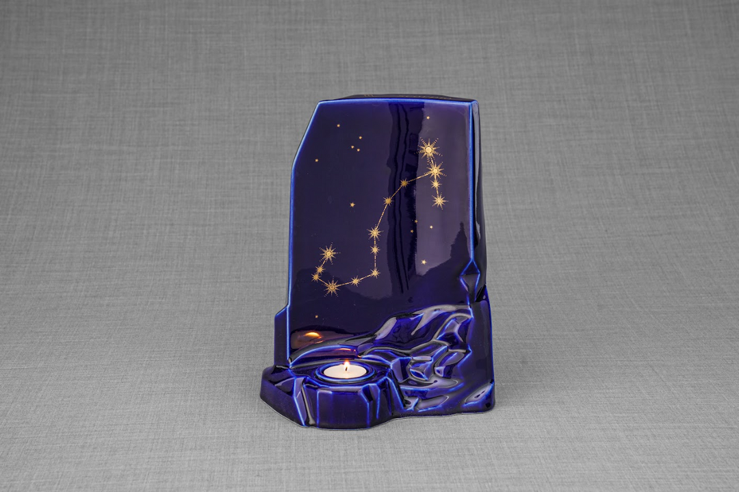 Blue Zodiac Ceramic Urn featuring a gold star constellation pattern with a candle holder against a gray backdrop.