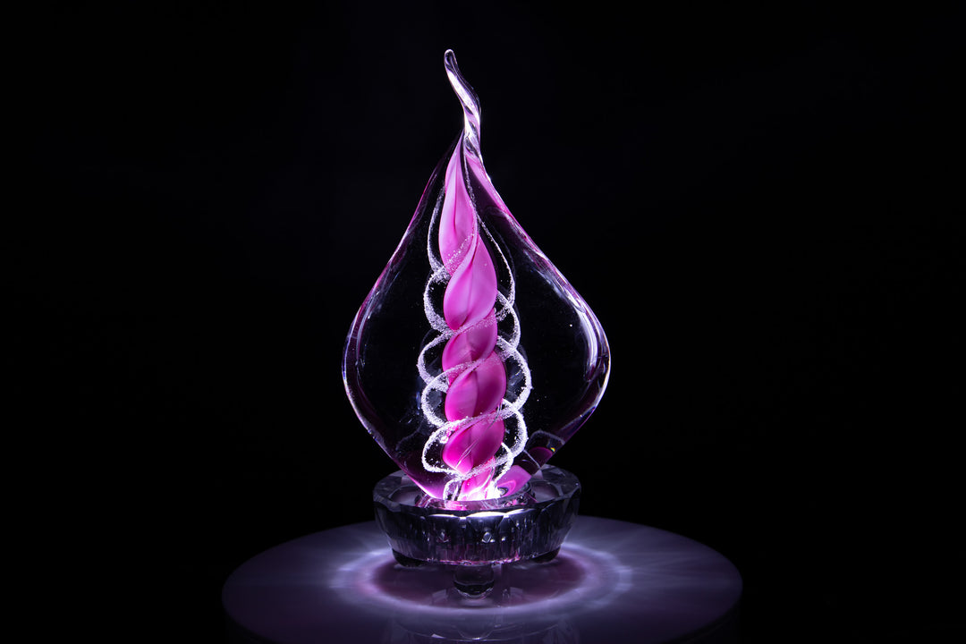 Purple glass memorial flame encasing cremation ashes with a pink spiral core glowing against a dark background.