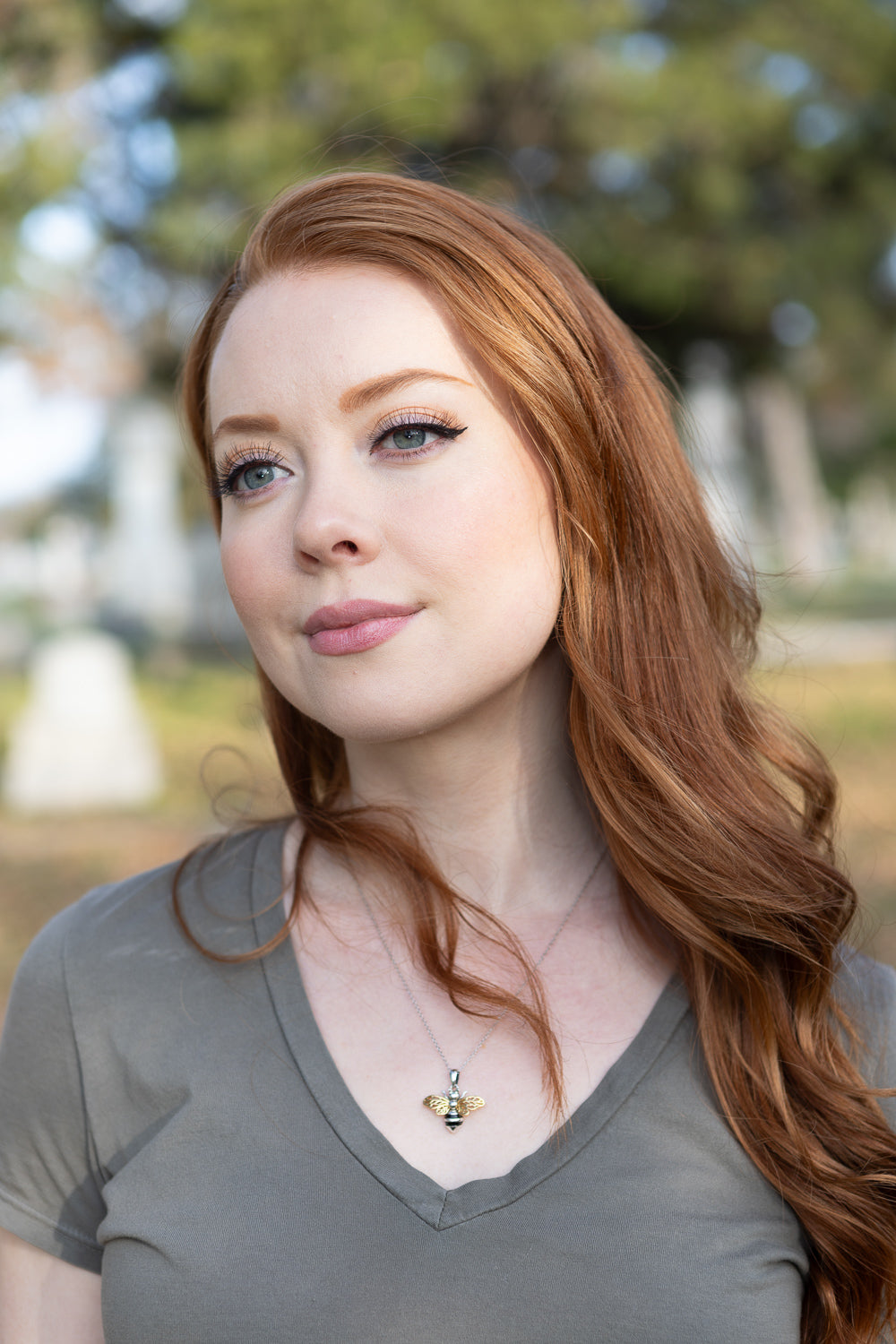 Red-haired woman wearing a bee keepsake urn pendant necklace on a silver chain