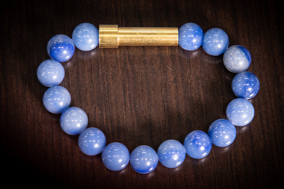 Blue apatite bead bracelet with a gold tube clasp on dark wood