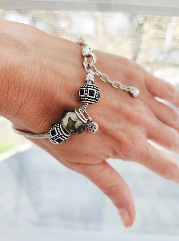 Silver charm bracelet on a wrist featuring a marbled green bead and ornate silver spacers