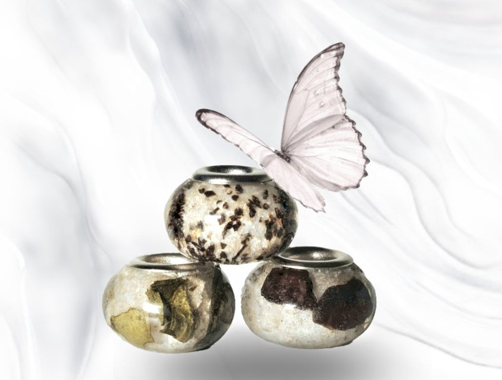 Three decorative beads stacked with gold leaf patterns and a pale butterfly perched above