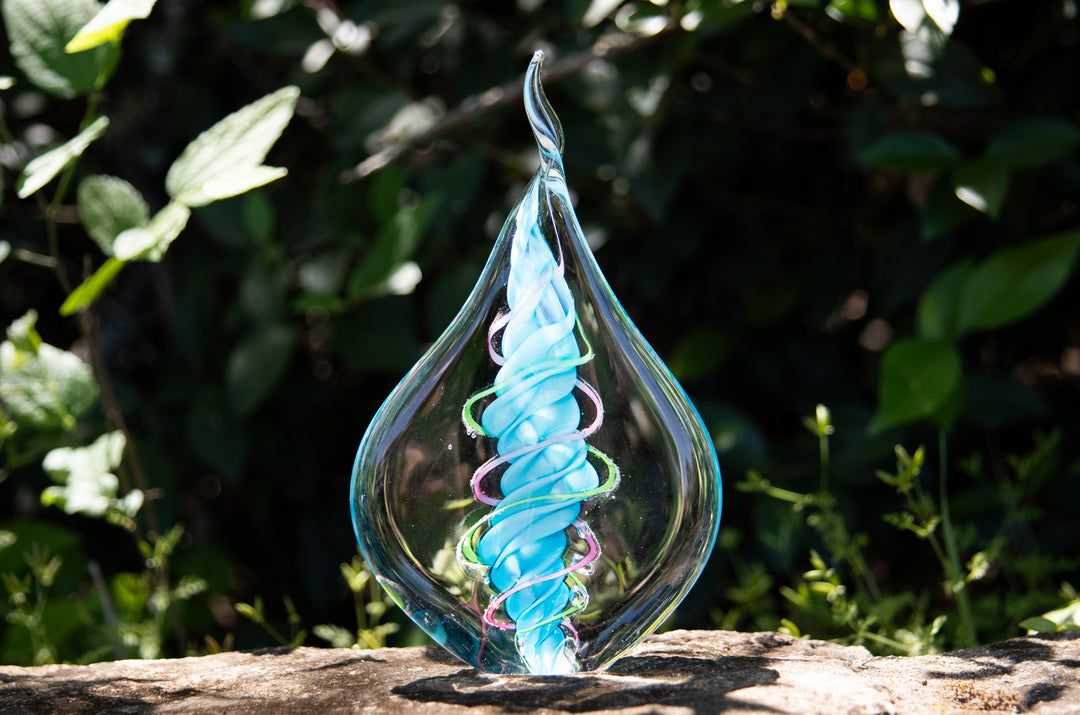 Clear glass teardrop memorial flame with two cremation ash spirals around a blue core.