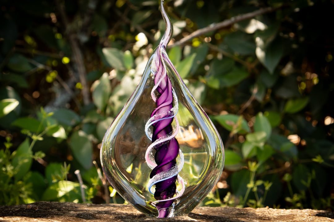 Dual memorial glass flame with two ashes spiraling around a purple core inside a clear teardrop vessel.