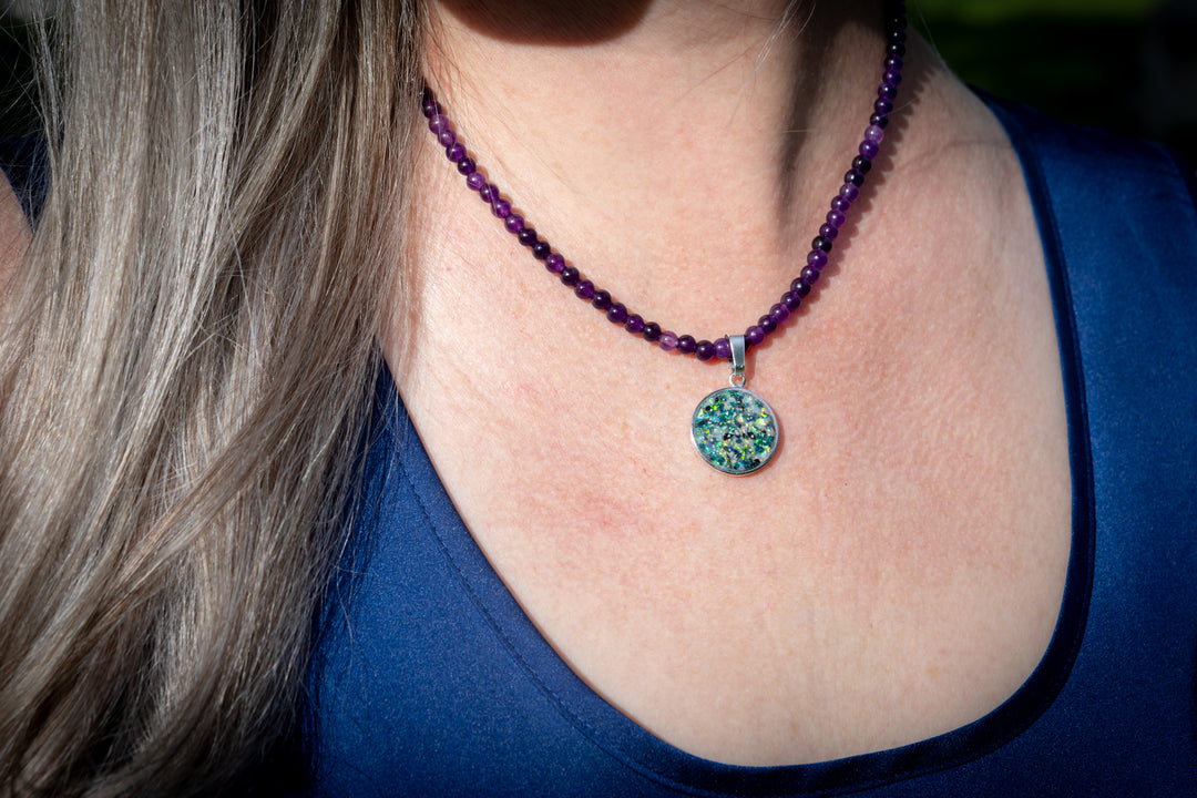 Close-up of a person wearing a purple beaded cremation necklace with a colorful pendant.