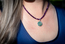 Close-up of a person wearing a purple beaded cremation necklace with a colorful pendant.