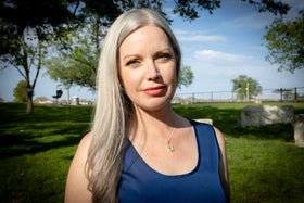 pendant with hair - Person wearing a blue top with a necklace featuring a yellow pendant outdoors.