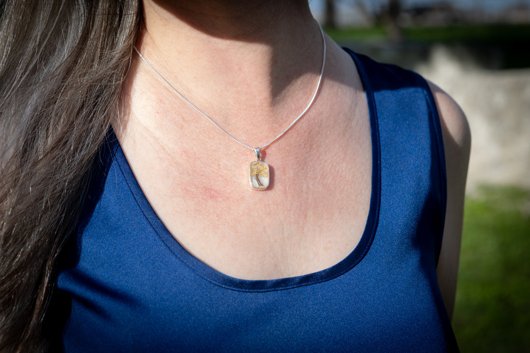 pendant with hair - Person wearing a blue top with a necklace featuring a yellow pendant outdoors.