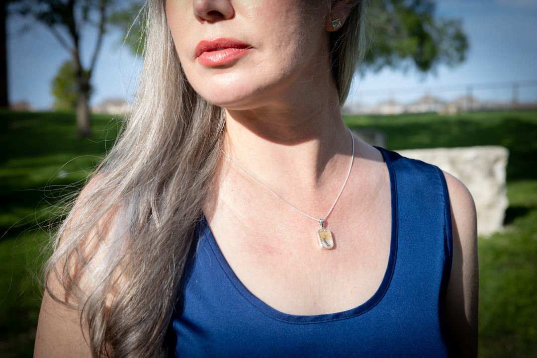 pendant with hair - Person wearing a blue top with a necklace featuring a yellow pendant outdoors.