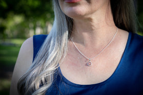 cremation pendant with ash on Woman with blonde hair and red lipstick looking to the side with a blurred green background