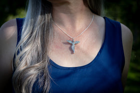 guardian angel pendant with ash worn on Woman with long blonde hair wearing a blue top and necklace in a park setting