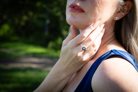 Woman wearing a cremation ring with cremation ash outdoors with greenery in the background