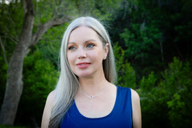 A woman wearing a silver cremation necklace with a heart pendant against a blurred background