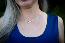 Person wearing a silver cremation necklace with a heart pendant against a blurred background