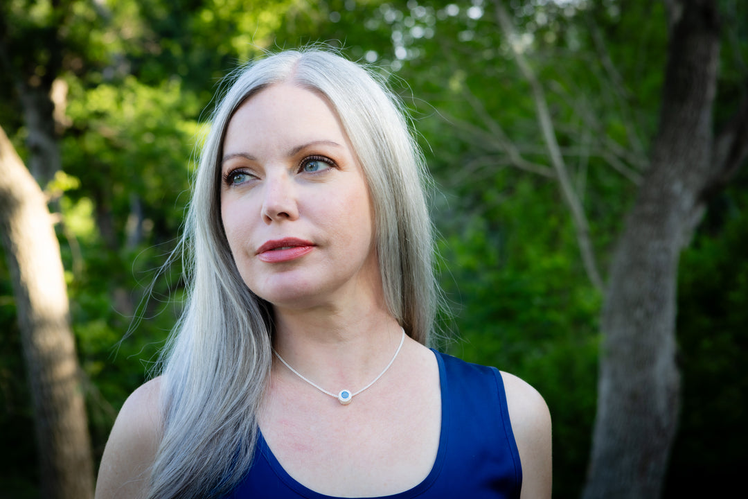 Woman wearing a cremation necklace from ashes of pets and people with long silver hair standing in a forest