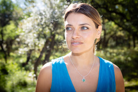 Woman wearing a blue top with a blurred natural background with celtic inspired cremation pendant - turquoise and lime green