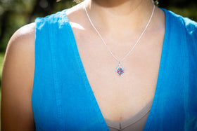 Woman wearing a blue top with a blurred natural background with Celtic inspired cremation pendant - red and blue