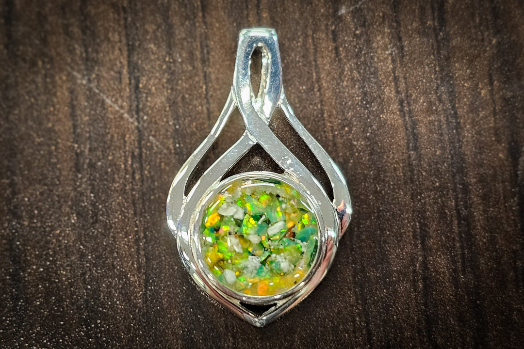 Silver Celtic Drop Pendant filled with cremation ashes and a colorful opal center photographed on dark wood