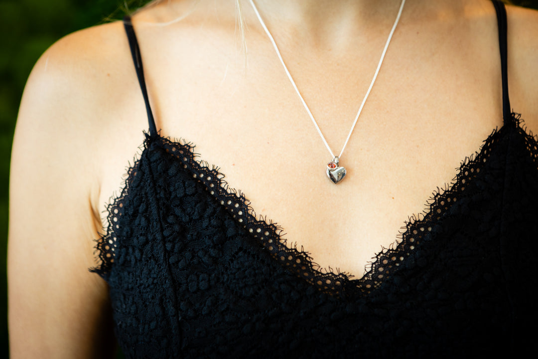 Silver heart cremation pendant with a birthstone crystal worn on a delicate chain at the collarbone.