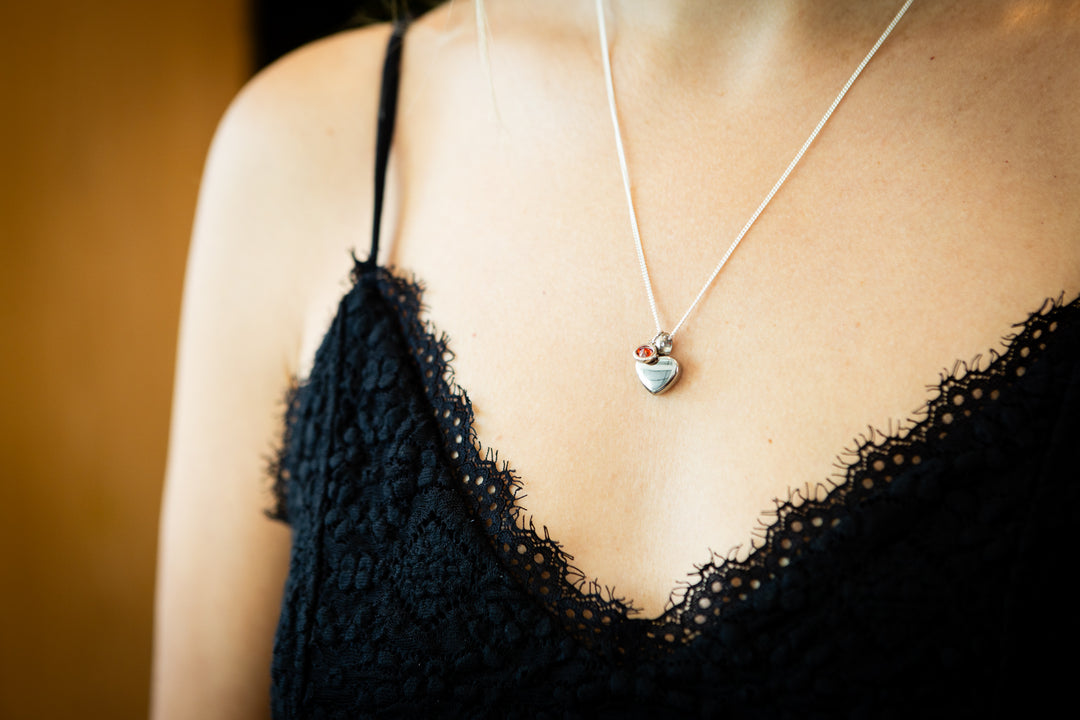 Silver heart keepsake cremation pendant with a small red birthstone crystal on a delicate chain.