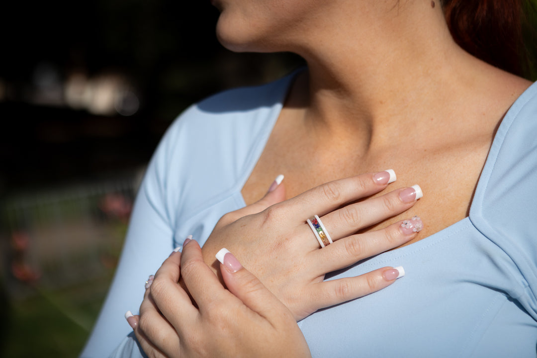 Model wearing a wide glass frit cremation ring with rainbow inlay between white edges on the ring finger