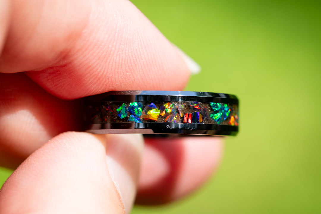 Black cremation ring and volcanic ash from Mt. Saint Helens with colorful gemstones on a textured surface