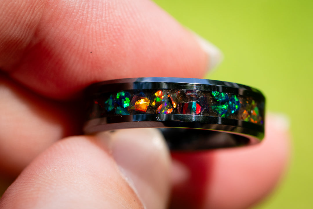 Black cremation ring and volcanic ash from Mt. Saint Helens with colorful gemstones on a textured surface