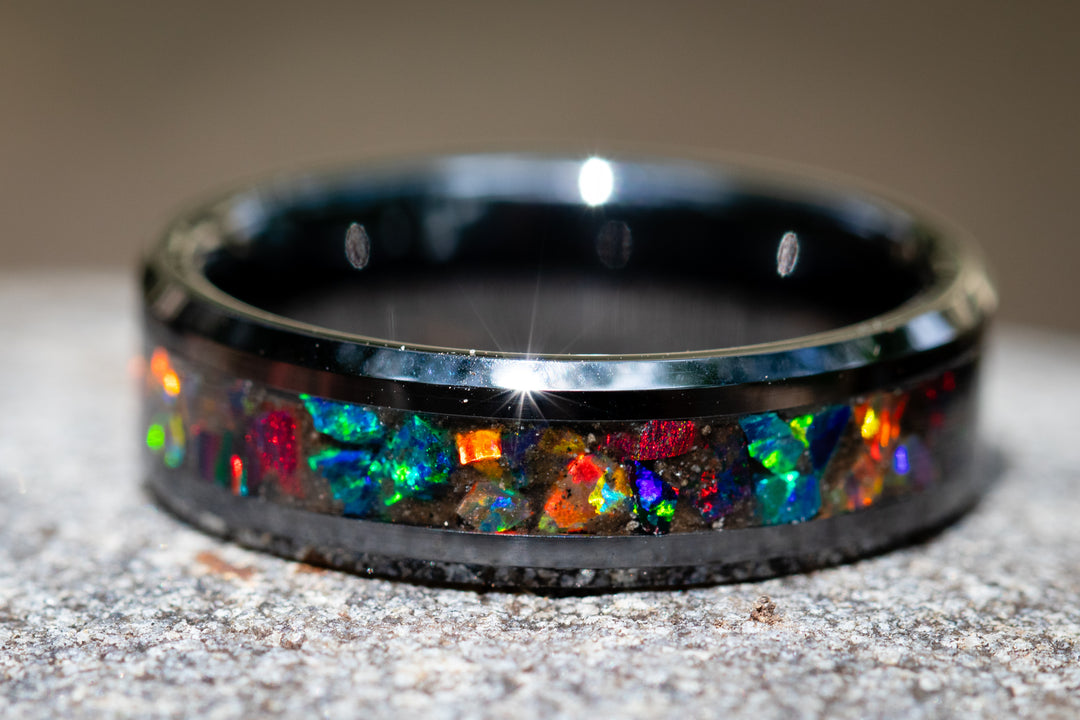 Black cremation ring and volcanic ash from Mt. Saint Helens with colorful gemstones on a textured surface - black opal mix