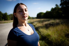 Woman standing on a road with grass and trees in the background wearing a cremation necklace