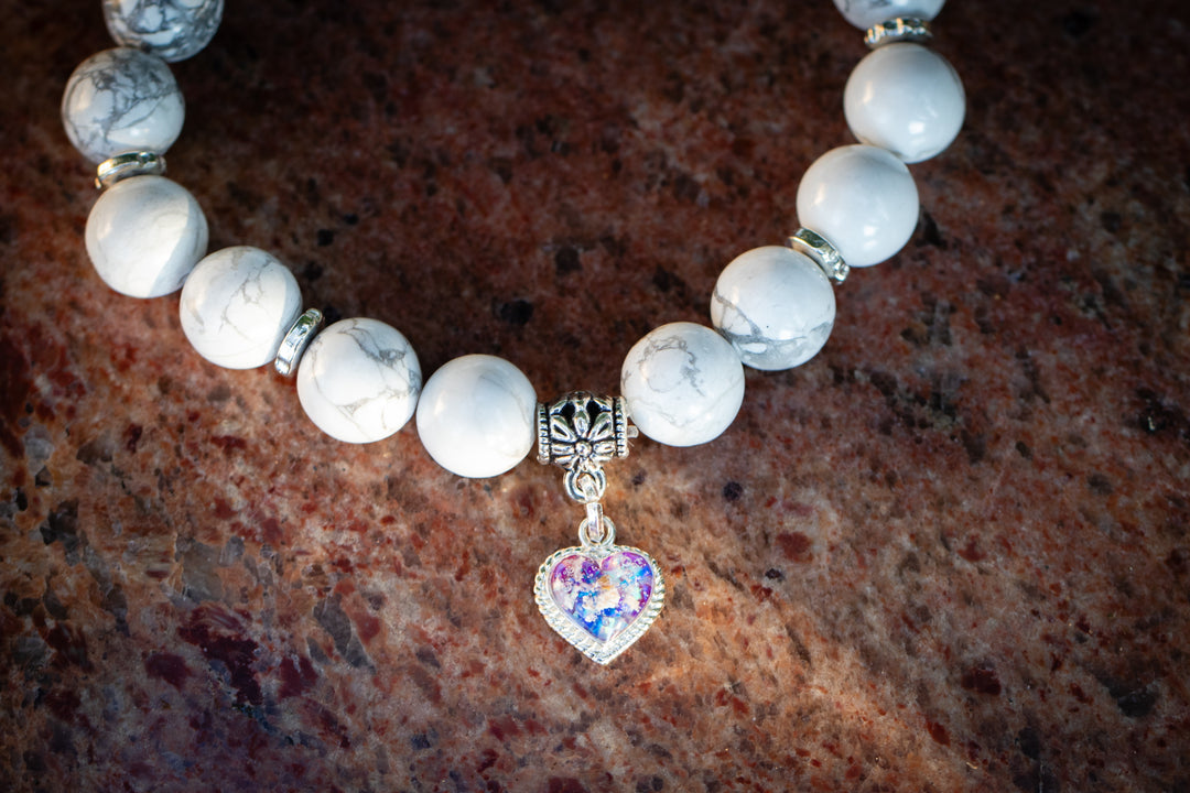 Howlite cremation bracelet with ornate silver centerpiece and heart charm on textured rock background