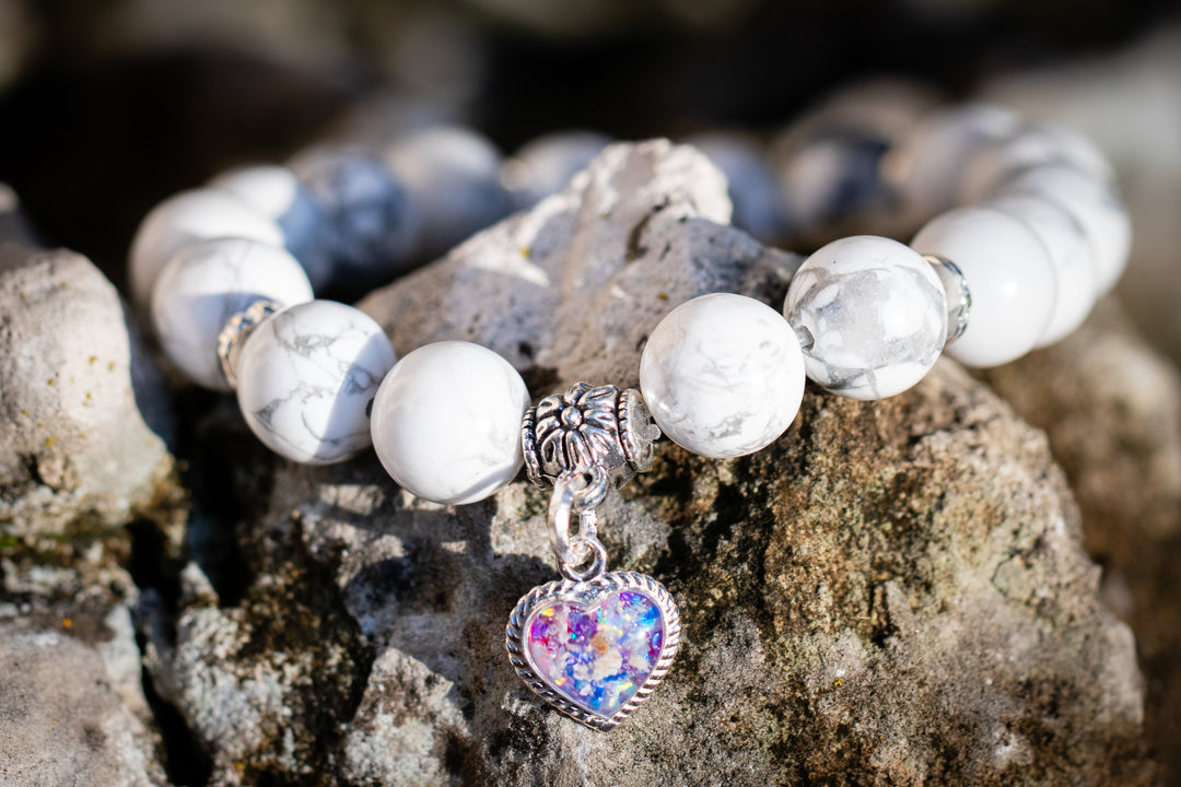 Howlite cremation bracelet with a colorful opal heart pendant on a rocky surface