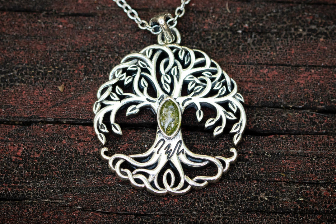 Silver tree of life pendant with a green gemstone on a dark wooden background