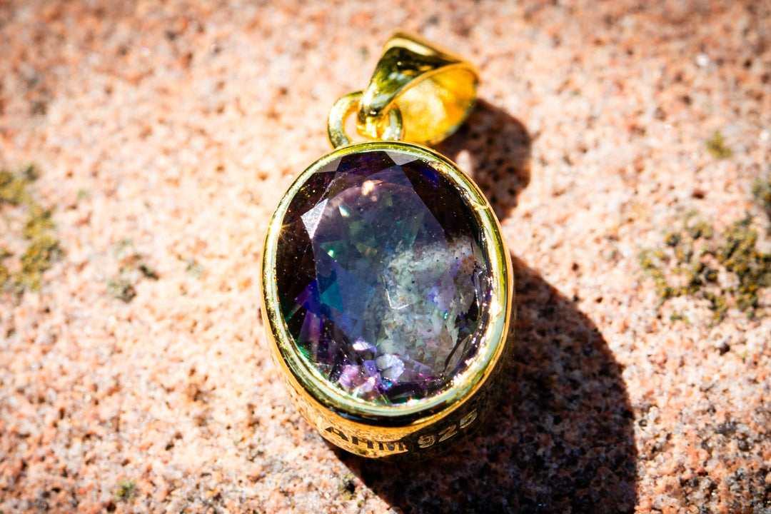 Gold cremation pendant with a purple gemstone on a textured stone surface - gold plate mystic topaz
