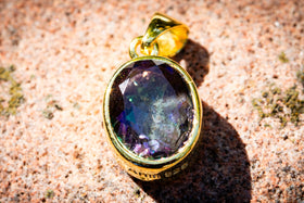 Gold cremation pendant with a purple gemstone on a textured stone surface - gold plate mystic topaz
