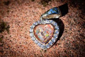 Heart-shaped opal pendant with diamond accents on a textured surface with cremation ash on pearl colored crushed opal - white (orange comes from stone background)