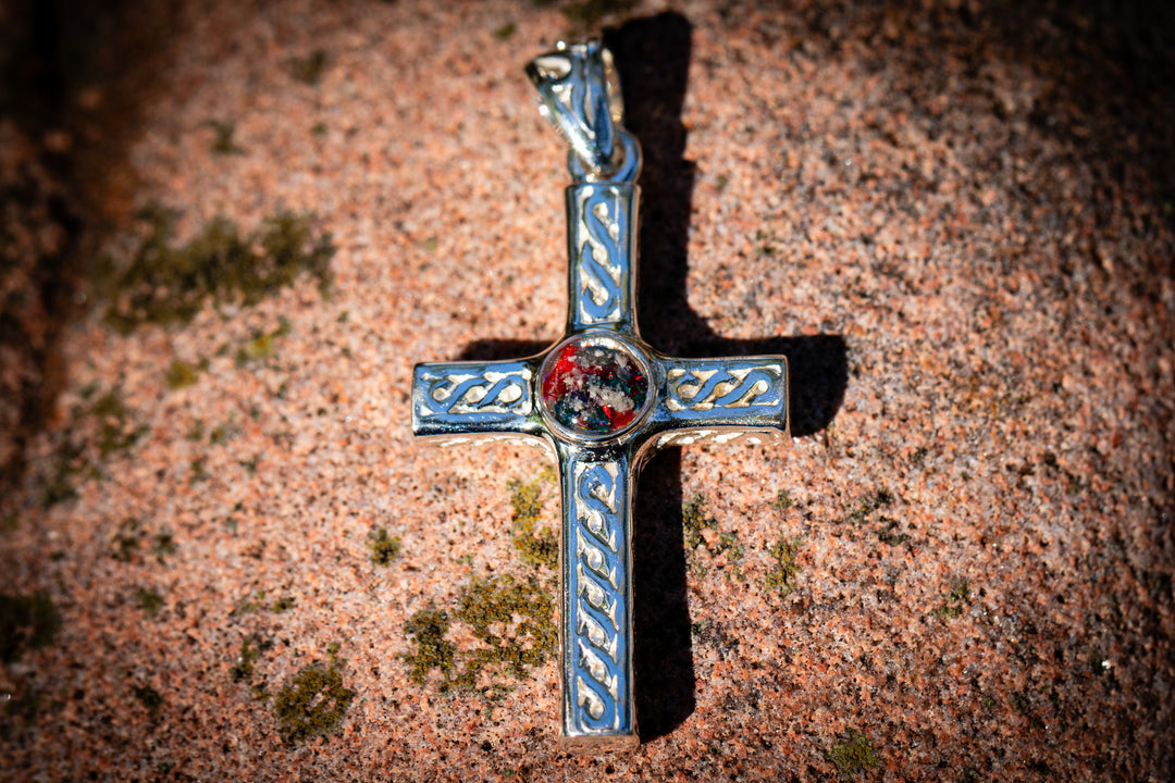 Decorative cremation cross pendant red and black for men and woman with a red gemstone on a textured brown surface