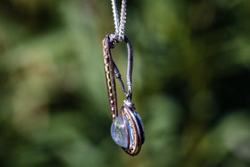 Close up of a Brizo pendant showing copper wire wrap around a blue glass cabochon on a silver chain.