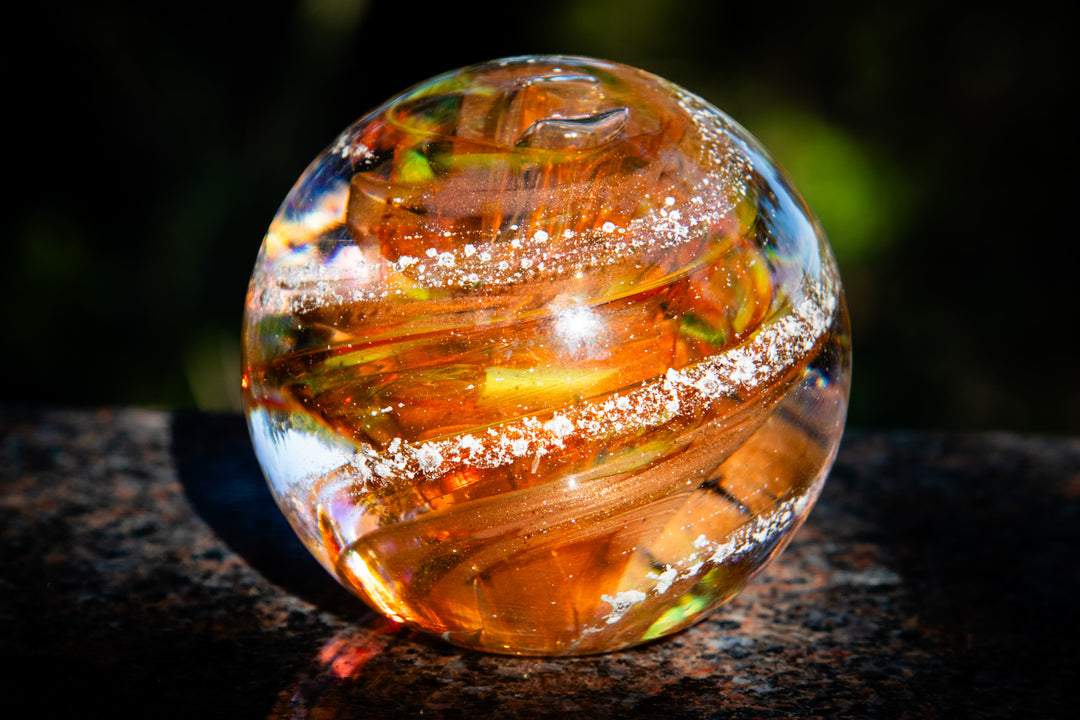 Clear glass cremation orb with internal patterns on a dark surface