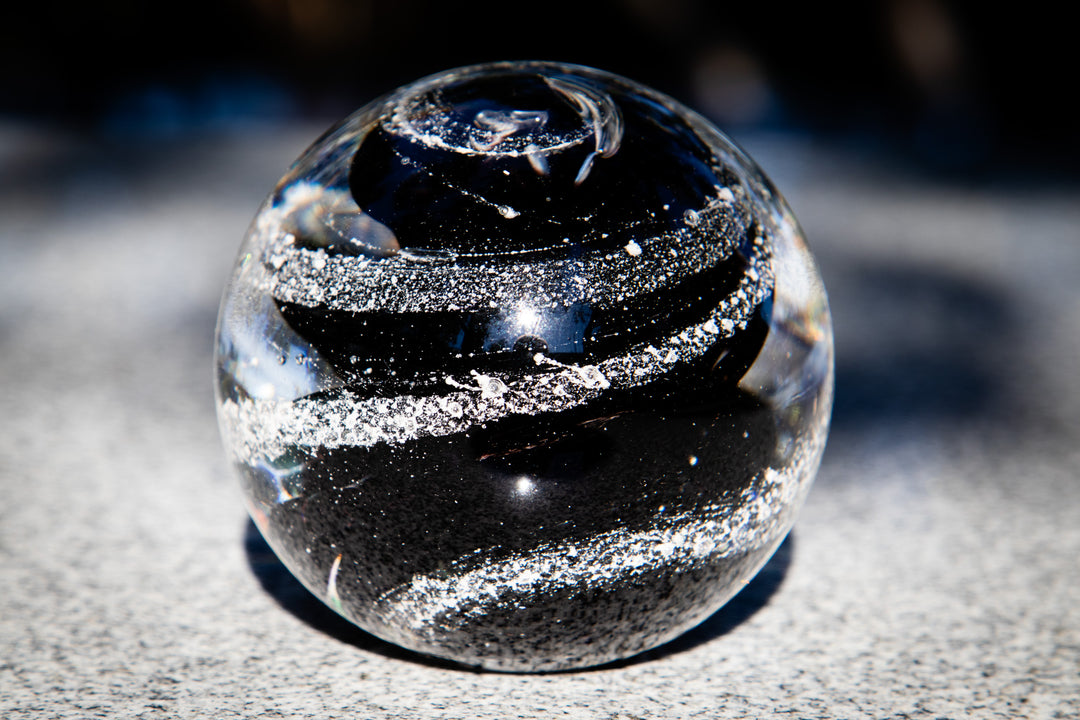 Blue swirl glass orb paperweight with cremation ashes, resting on a dark blurred background.