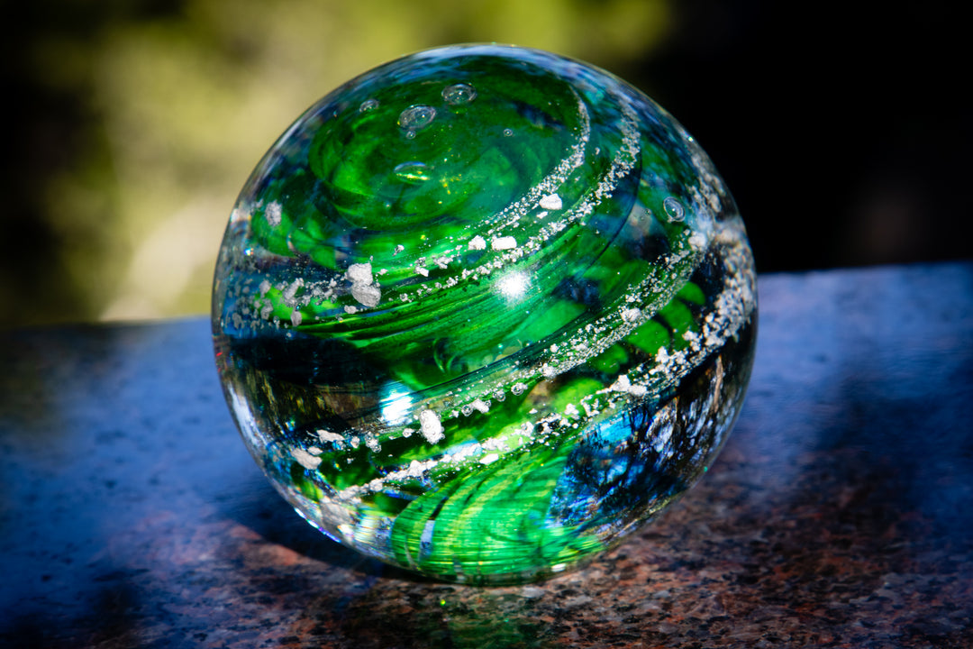 Green Sparkle Orb with swirling emerald ribbons and silver glitter on a dark granite surface.