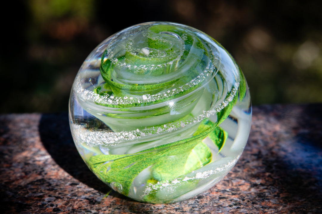 Green swirl glass paperweight with ash inclusions on a dark stone surface
