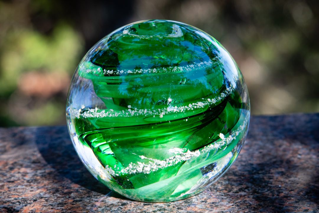 Bright green glass swirl paperweight with ash accents resting on a granite surface outdoors