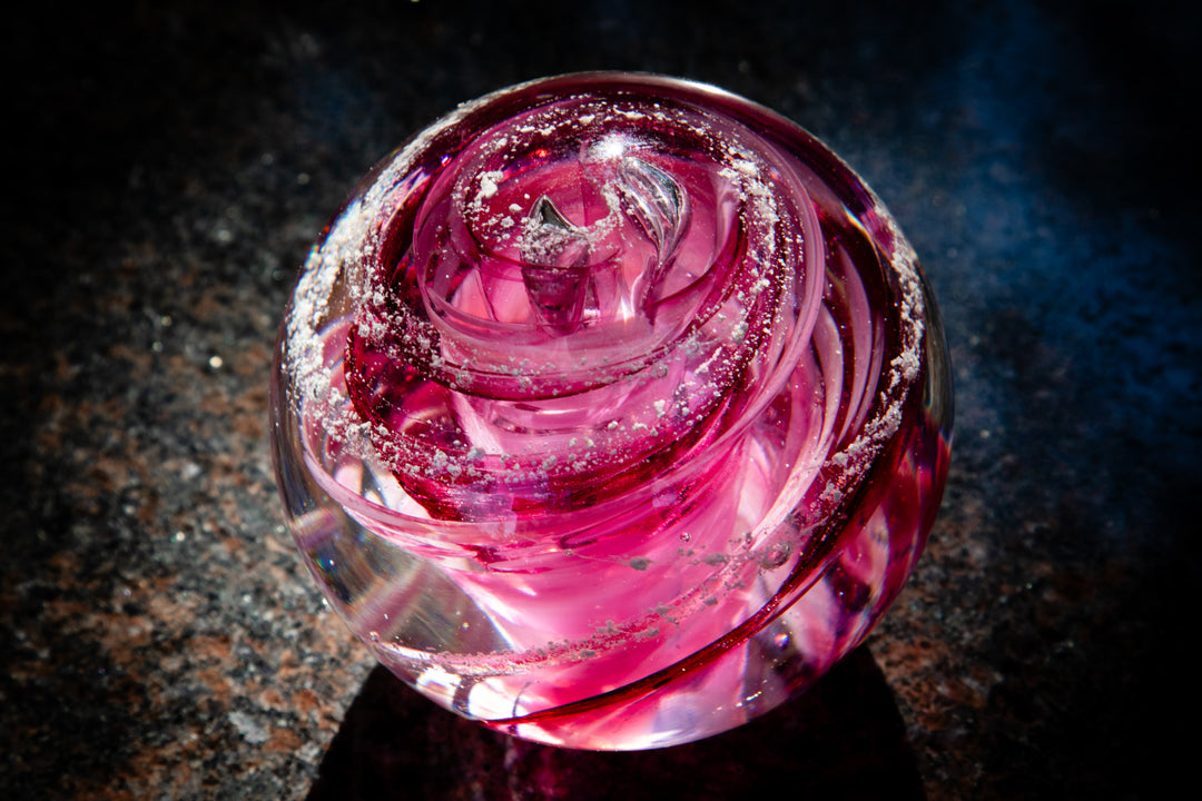 Pink tranquil swirl glass paperweight infused with cremation ash featuring curved ribbons and speckled accents
