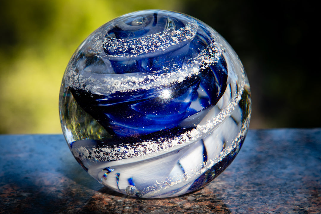 Deep blue solid glass orb infused with cremation ashes and bright swirls