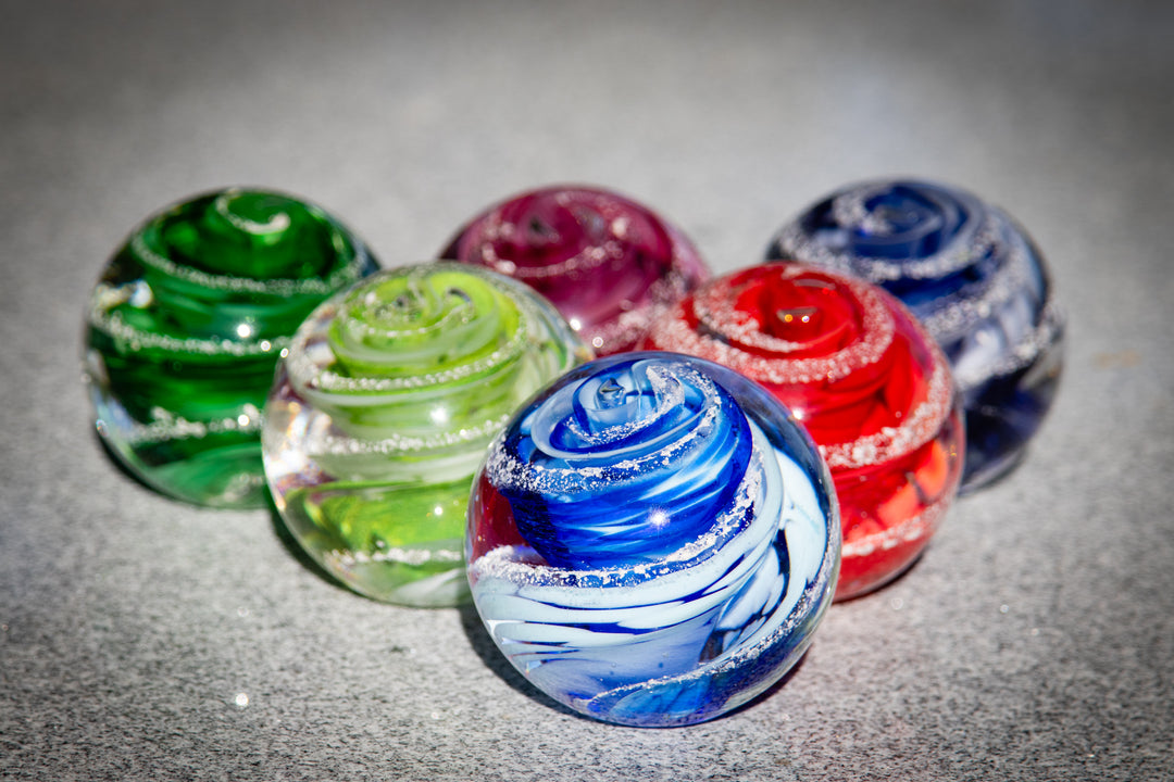 Group of vibrant glass swirl paperweights with ash accents on a gray surface