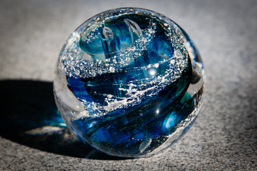 Blue Tranquil Swirl Orb close up with white speckles on a neutral surface