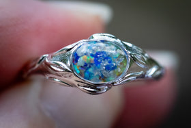 Silver ring with a colorful opal stone held between fingers.  Blue white and yellow