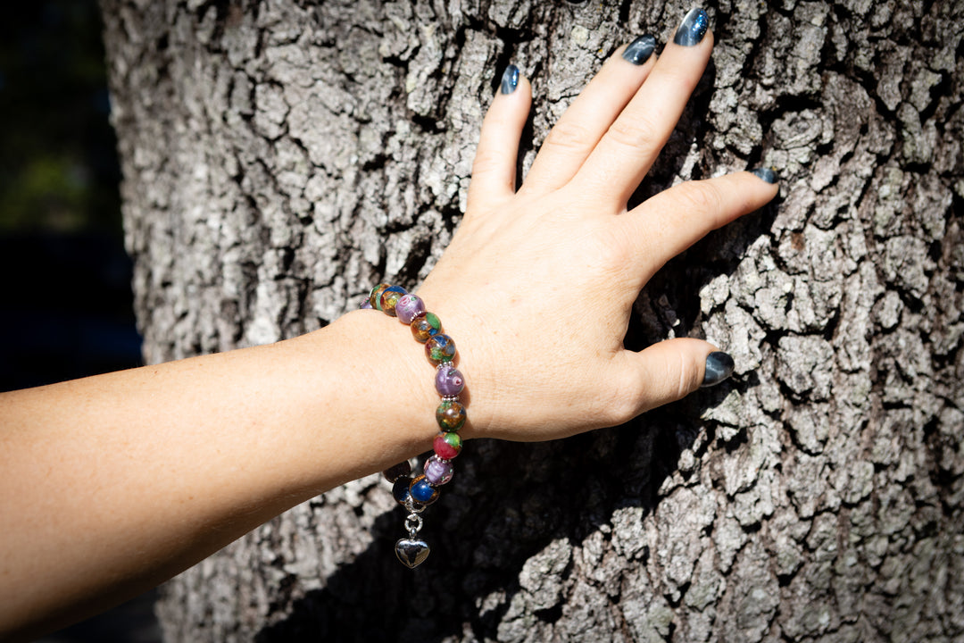 Hand with a colorful beaded bracelet on a tree trunk