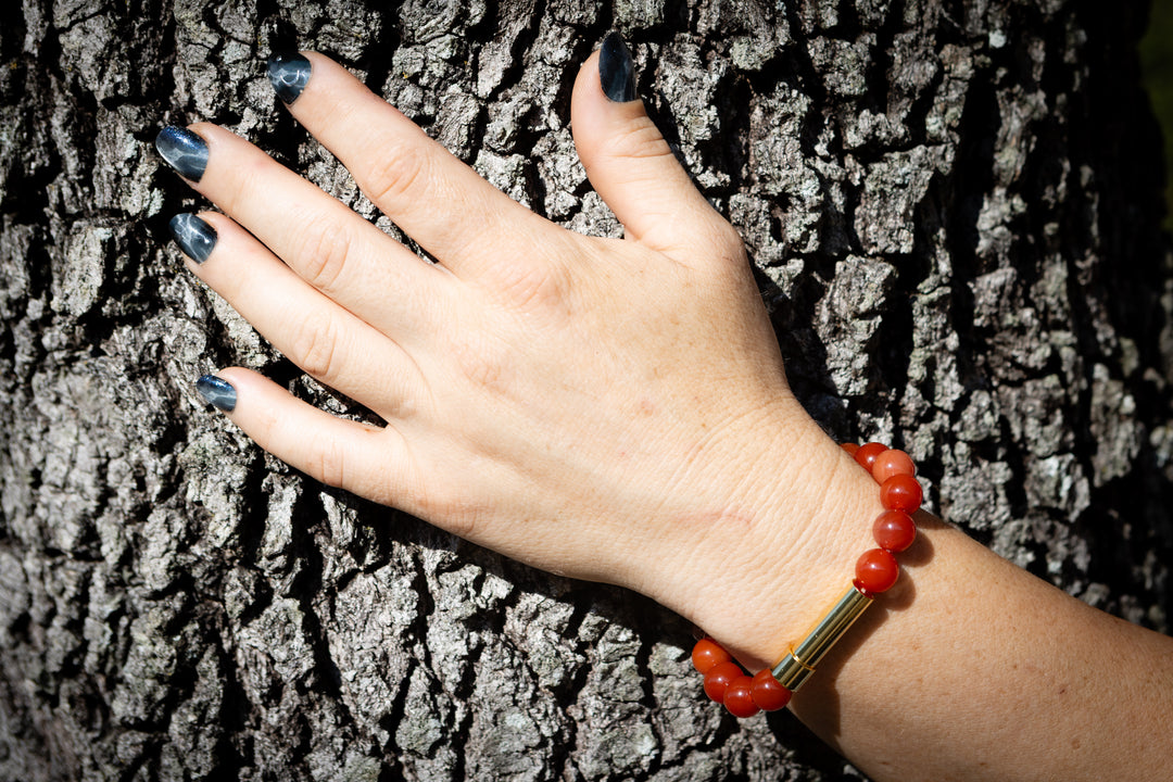 Carnelian cremation bracelet with red beads and a gold tube clasp worn on the wrist